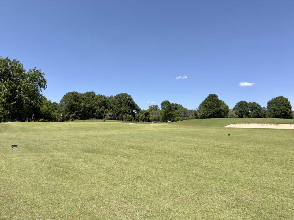 Washington Monument framed through the tree line from the 2nd fairway at East Potomac White Course, greenside bunker on the right