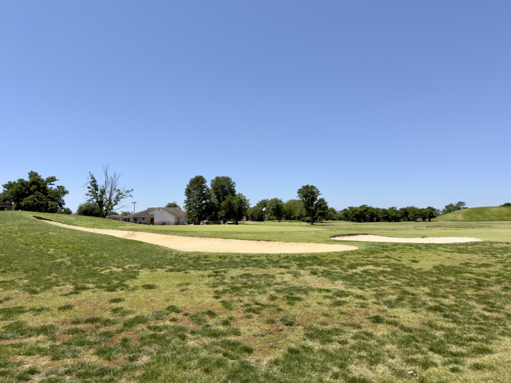 Seventh green at East Potomac White Course, sand bunkers left and right, maintenance facility in the background