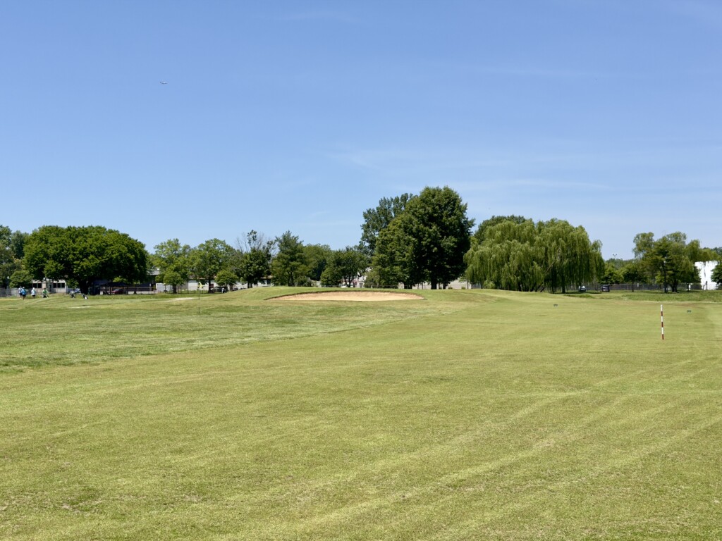 Approach to the 8th green at East Potomac White Course from 120 yards, large bunker fronting the green, plane overhead