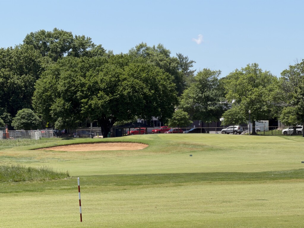 Eighth green at East Potomac White Course, large bunker dug into the front-left, parking lot and tree line behind