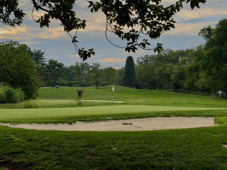 View from behind the 14th green at Herndon Centennial Golf Course, back bunker in the foreground and a pond front-left of the putting surface.