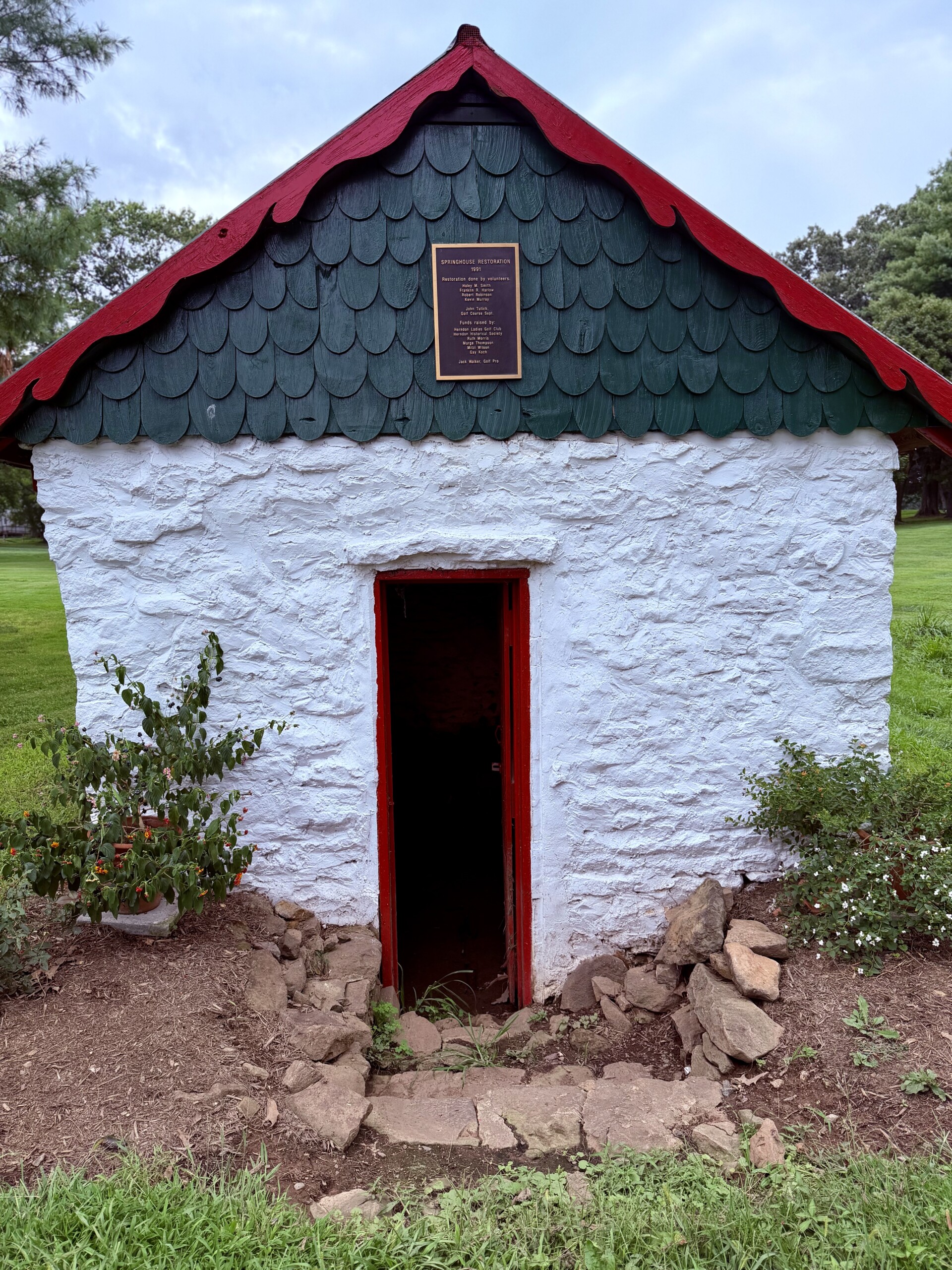 Restored springhouse along the 4th hole at Herndon Centennial Golf Course, whitewashed stone with a green scalloped gable.